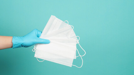 Hands holding face masks wear blue medical gloves on mint green or Tiffany Blue background.