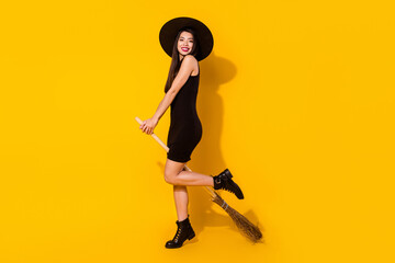 Photo of positive cheerful girl hold broom posing wear witch costume short dress isolated on yellow...