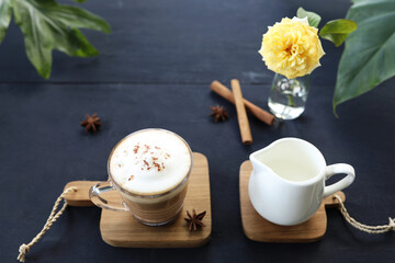 Latte coffee in glass cup and milk pitcher with rose flower on dark table