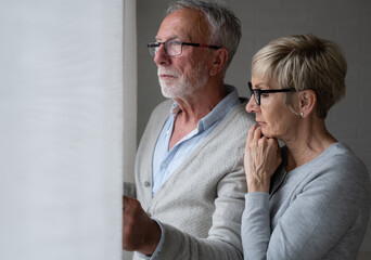 Senior retired couple looking sad through the window of their home