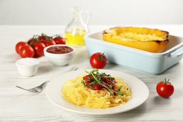 Tasty spaghetti squash with tomato sauce and arugula served on white wooden table