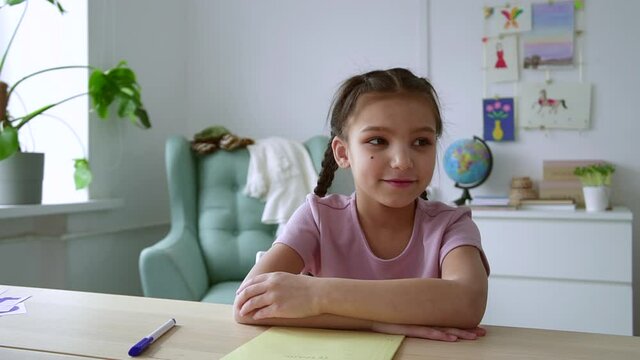 Home distance schooling for kids. Spbd Happy little girl with mole on cheek nods head and talks at videochat at table in children room camera view