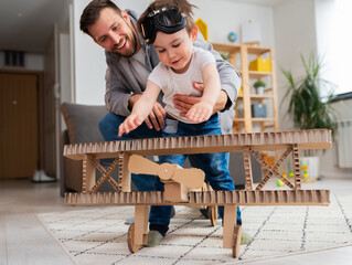 Father playing with toddler son. Playing on the floor with cardboard airplane