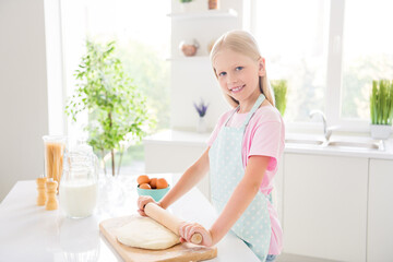 Photo of positive happy small girl hold rolling pin make pizza dough smile indoors inside house home kitchen
