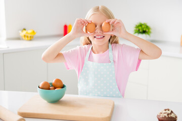 Photo of young happy positive small girl smile cover eyes eggs smile chef wear apron indoors inside...