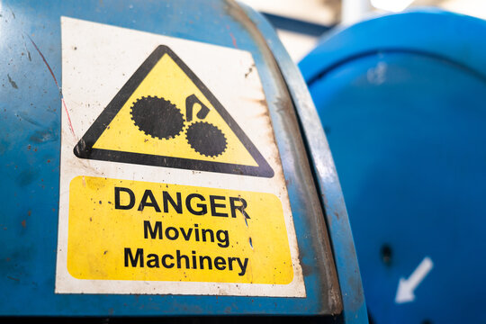 "Moving machinery" danger caution sign on the heavy machine in the factory. Industrial safety operation sign-symbol photo. Close-up and selective focus.
