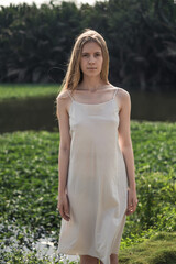 Portrait of attractive young caucasian woman in white dress standing in the park. Long blond hair. Natural beauty. Make-up free. 