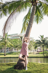 Pretty girl in casual clothing leaned on palm tree in the park. Long blond hair. Trendy casual summer or spring outfit
