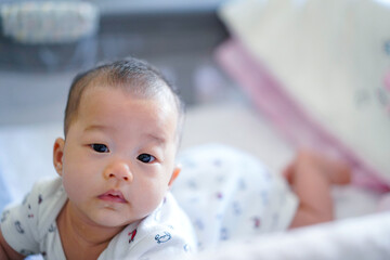 Innosence baby is crawling on bed sheet in bedroom. Baby look at front Asian baby girl is seven months old.