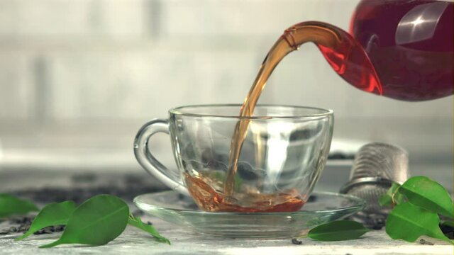 Super slow motion from the teapot is poured into a cup of black tea. On a white background. Filmed on a high-speed camera at 1000 fps.