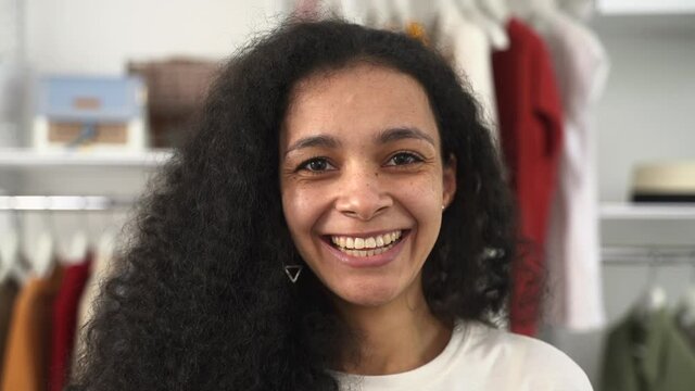 Wardrobe with contemporary garment keeping supplies. Spbd Attractive African-American woman with long curly hair smiles into camera near rack in walk-in closet closeup