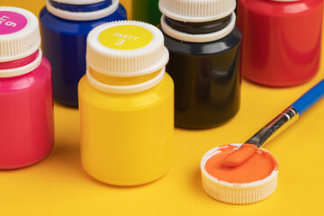 Jars with acrylic paint and brush on yellow background
