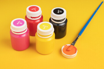 Jars with acrylic paint and brush on yellow background
