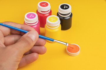 Jars with acrylic paint and brush on yellow background