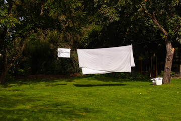 Du linge blanc s&egrave;che sur un fil entre deux arbres dans un jardin