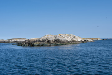 A picture of a beautiful rock island. Ocean and blue sky in the background. Picture from the Weather Islands, on the Swedish West coast