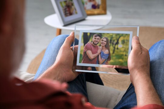 Senior man holding frame with photo of young couple at home, closeup