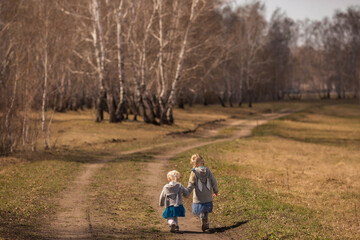 little girls girlfriends holding hands walking through a birch grove