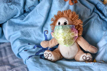 A teddy bear in a medical protective mask on a bed