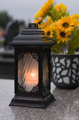The lantern with candle and flowers as a decoration on the marble grave.
