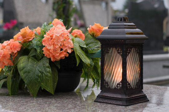 The lantern with candle and flowers as a decoration on the marble grave.