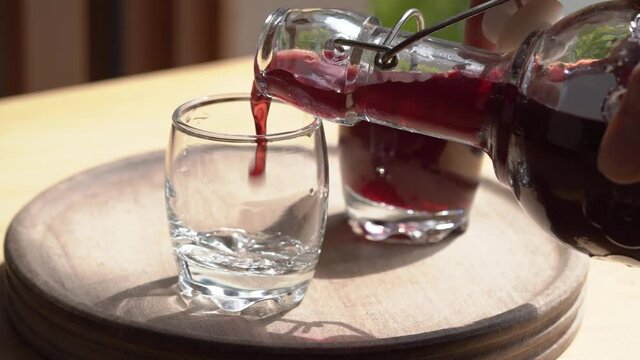Pouring homemade black elder syrup from a bottle into a glass, slow motion