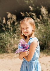 Beautiful little girl in a blue dress with flowers in nature in the summer