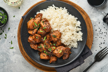 Spicy teriyaki chicken fillet pieces with rice, green onions and black sesame seeds on black plate on a grey slate, stone or concrete background. Top view with copy space. © kasia2003