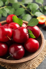 Delicious ripe cherry plums with leaves on black table, closeup