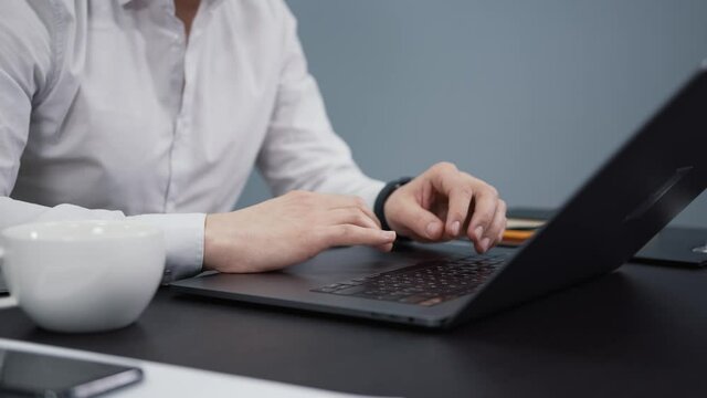 Businessman with laptop and phone on the table, man fingers typing on the laptop, closeup. Manager working in office with devices and cup of coffee, gimbal shot
