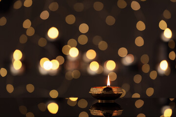 Lit diya on table against blurred lights, space for text. Diwali lamp