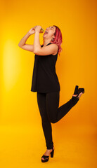 the girl standing on one leg, lifting up the other greedily biting a fragrant burger on a yellow background in black clothes. Fast food advertising