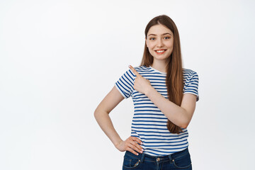Young smiling woman pointing finger at upper left corner, empty space for shopping sale advertisement, standing over white background