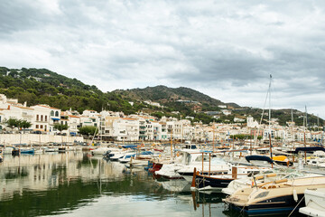 Fototapeta na wymiar View of small spanish town of Port de la Selva harbor in the Costa Brava in Catalonia, with small white fishing boats on a cloudy summer day during tourist season.