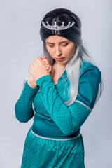 Portrait of a princess in a medieval, fantasy, turquoise dress with ash hair and a silver crown, posing hands folded in prayer isolated on a white background.