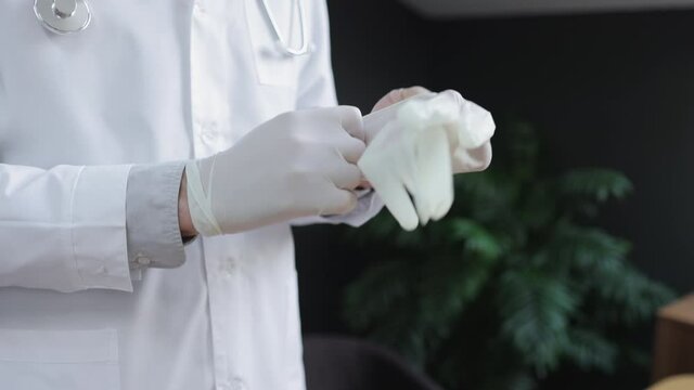 Male doctor putting on gloves and standing in interior of clinic during working day spbi. Close-up view of young man professional puts on sterile gloves on hands and poses, stands in light room. One