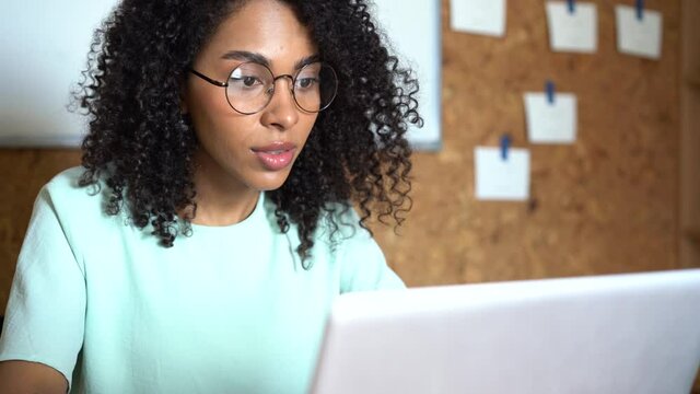 Thinking mixed-race businesswoman working on laptop computer in office interior