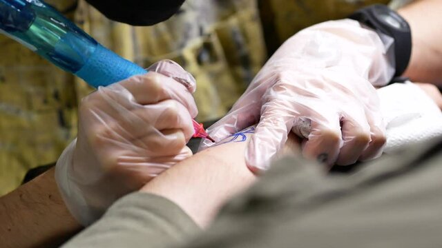 Male tattooist making tattoo on hand of client