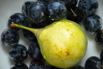 ripe yellow pear and plums in water on the table at home, one pear