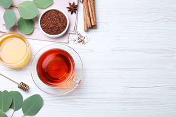 Freshly brewed rooibos tea, dry leaves, honey and spices on white wooden table, flat lay. Space for text