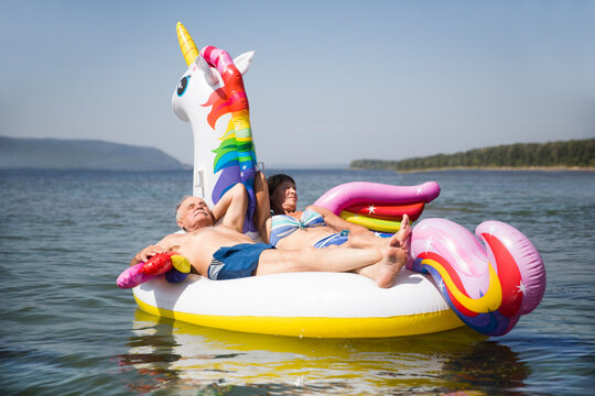 Happy older couple swim Inflatable Unicorn on a sunny day on the beach holiday
