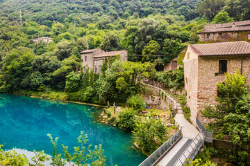 A glimpse of the small village of Stifone, on the Nera river. Umbria, Terni, Italy. The walls of stones and bricks. The bridge over the river with clear blue waters. Tourists stroll through the alleys - obrazy, fototapety, plakaty