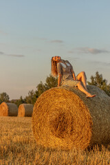 Young woman in blue dress close up on the field background with haystacks at sunset time.
