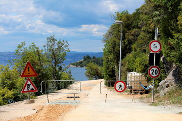 Closed road under construction with various road signs from 20 speed limit and 5t weight limit to warning road works ahead road signs at start of construction site surrounded with protective metal fen