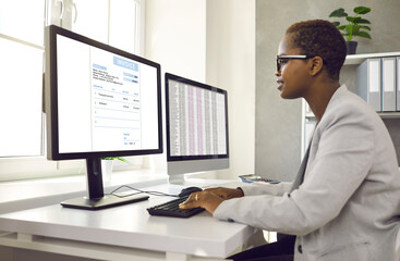 African American female accountant working with software for electronic invoices on computer. Side...