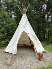 Tepee in the forest with wood logs as seats, ancient and traditional habitat of the first nations. Old tipi camp. © Stephanie