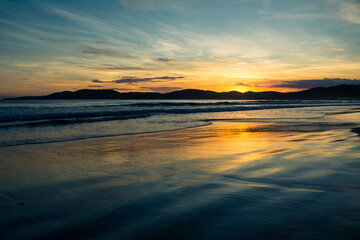 Fototapeta na wymiar Nascer do sol na praia com nuvens, reflexo e ondas - Paisagem natural