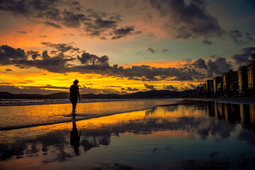 Fototapeta na wymiar Pessoa caminha ao nascer do sol laranja com lindo reflexo em Itapema - Paisagem natural