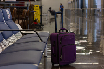 Obraz na płótnie Canvas Unattended small carry on lugagge by empty bench seats at airport terminal. Purple suitcase left alone, security hazard concepts
