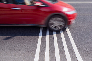 Rumble strips or speed breakers  on asphalt road surface and red car crossing them in motion blur. Traffic calming concept.